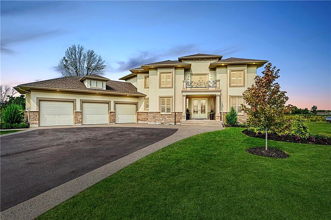 Front exterior of a finished custom home at dusk with stone, stucco and iron balcony